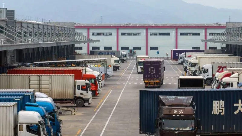 مستودع شحن يحتوي على شاحنات نقل متوقفة، يعكس تأثير التعريفات الجمركية على سلاسل التوريد العالمية للملابس.