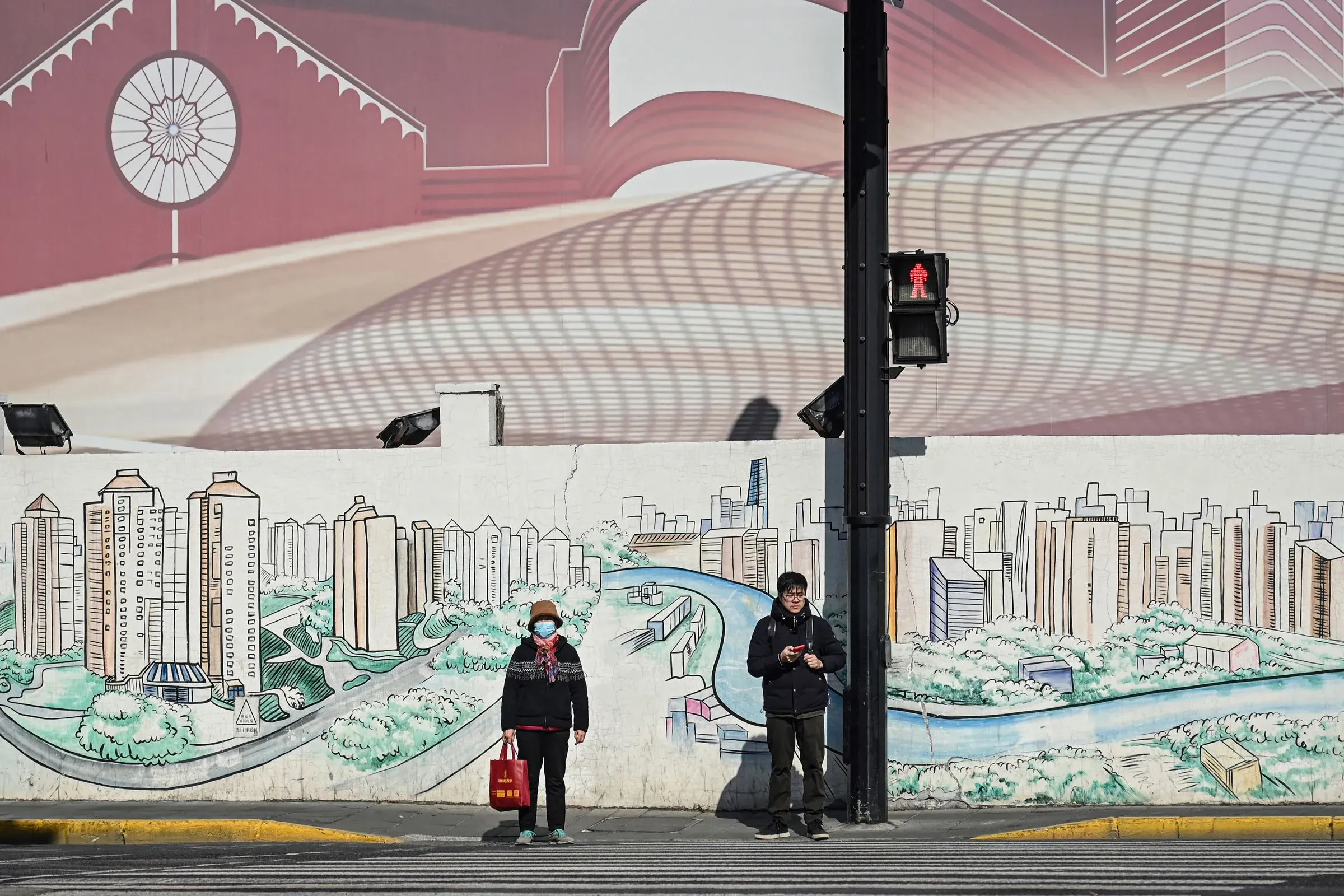 رجل وامرأة يقفان عند إشارة مرور أمام جدار مزخرف برسوم تعكس الحياة الحضرية في الصين، مما يعكس التحديات الديموغرافية الحالية.