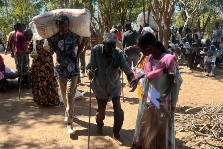 مشهد من منطقة تيغراي يظهر أشخاصًا يتلقون المساعدات الإنسانية، مع التركيز على رجل مسن يتلقى الدعم من شاب، في ظل ظروف صعبة.