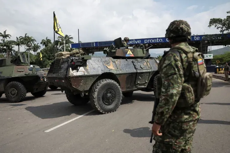عربة مدرعة تابعة للجيش الكولومبي في نقطة تفتيش، مع جنود في الخلفية، تعكس التوترات العسكرية المتزايدة في كولومبيا.
