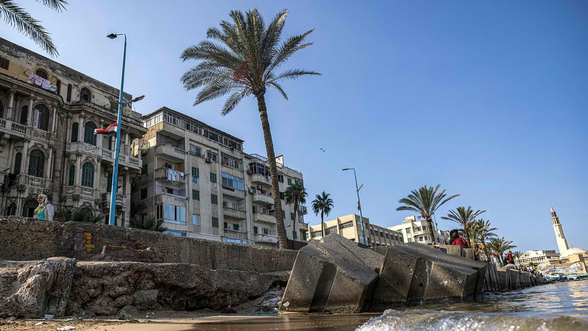 انهيار جزء من الرصيف في الإسكندرية، مع ظهور مبانٍ قديمة وحديثة، مما يعكس تأثير ارتفاع منسوب مياه البحر على المدينة.