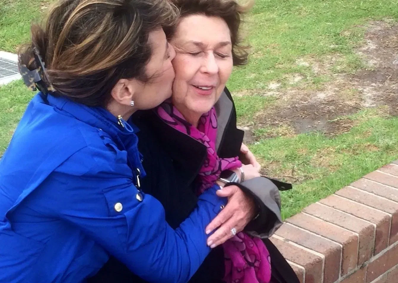 امرأة تحتضن وتقبل والدتها، التي ترتدي وشاحًا ورديًا، في مشهد يعكس الحب والقلق وسط عملية البحث عن نانسي غوثري المفقودة.