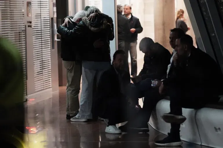 مشهد يعكس مشاعر القلق والدعم، حيث يحتضن شخصان بعضهما في مكان عام بينما يجلس آخرون في الخلفية، في سياق حادث إطلاق النار على المرشح الرئاسي الكولومبي.