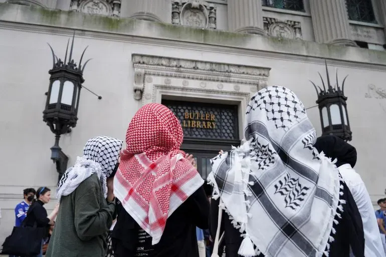 طلاب يرتدون الكوفية الفلسطينية يقفون أمام مكتبة بتلر في جامعة كولومبيا، تعبيرًا عن دعمهم للاحتجاجات ضد الحرب على غزة.