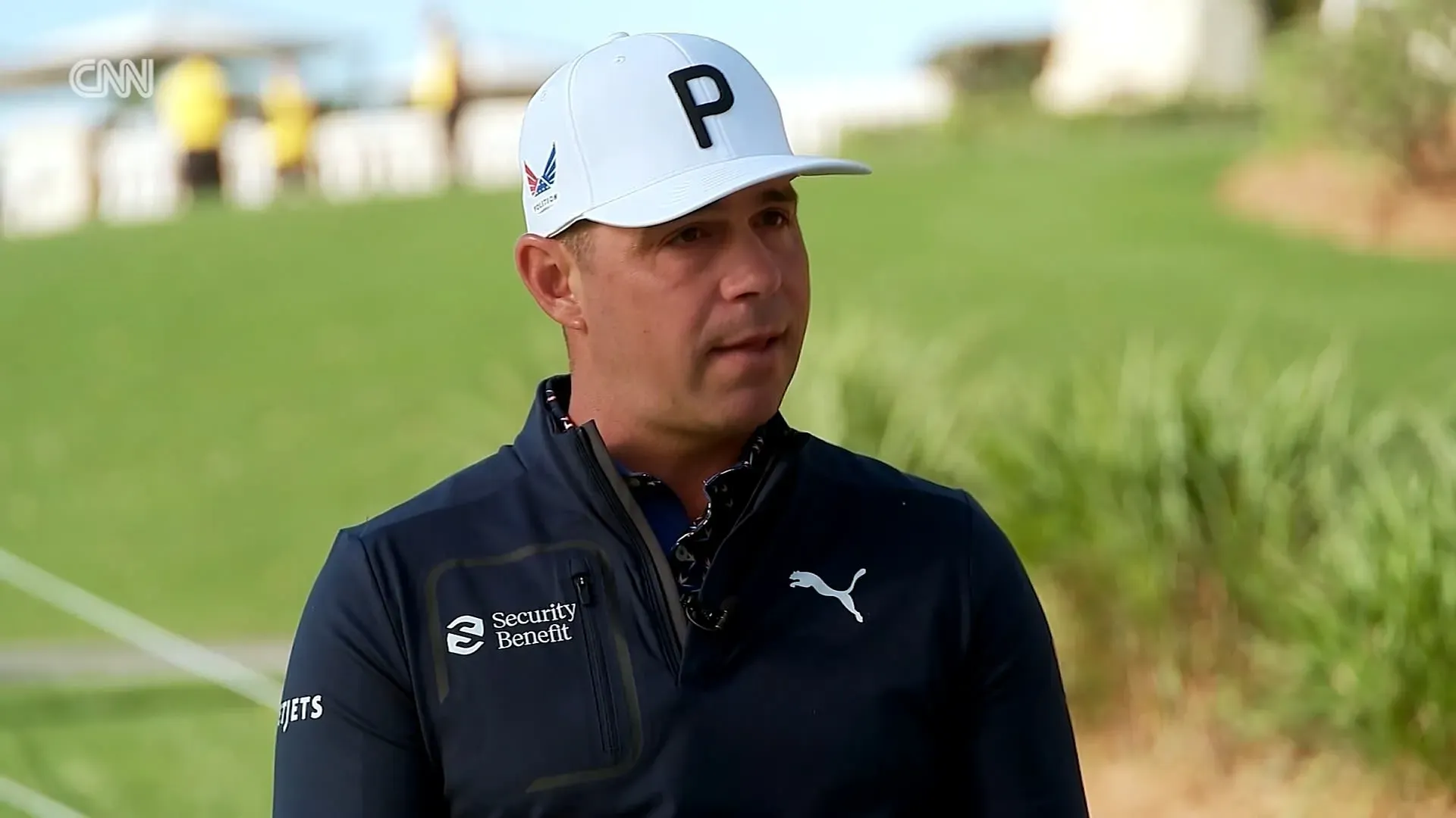 لاعب الغولف جاستن توماس يتحدث في مقابلة، مرتديًا قبعة بيضاء وقميصًا داكنًا، مع خلفية خضراء من ملعب الغولف.