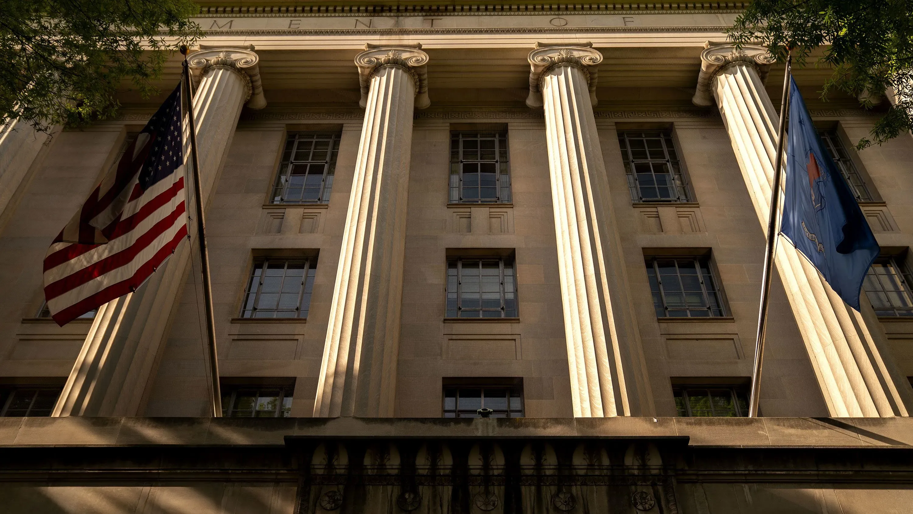 واجهة مبنى وزارة العدل الأمريكية، مع أعمدة بارزة وعلم الولايات المتحدة وعلم نيويورك، تعكس التوترات السياسية الحالية.