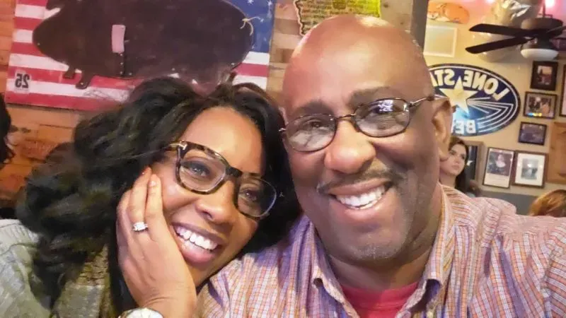 صورة لزوجين مبتسمين يجلسان معًا في مكان غير محدد، يعكسان لحظة من الألفة والفرح وسط تحديات الرعاية.