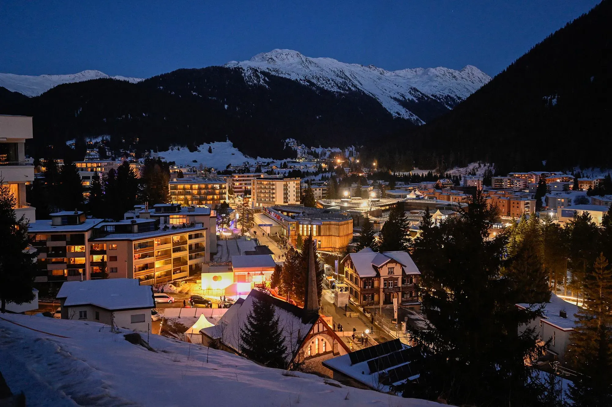 منظر ليلي لمدينة دافوس السويسرية، مع إضاءة المباني المحيطة والجبال المغطاة بالثلوج في الخلفية، يرمز إلى منتدى دافوس الاقتصادي.