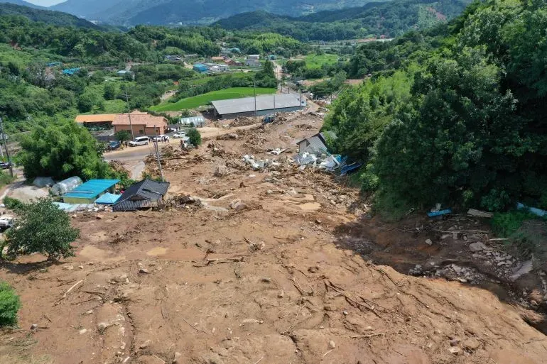 أرض مدمرة نتيجة انهيار أرضي في كوريا الجنوبية، مع بقايا منازل ومرافق محطمة، تعكس آثار الأمطار الغزيرة والتغير المناخي.