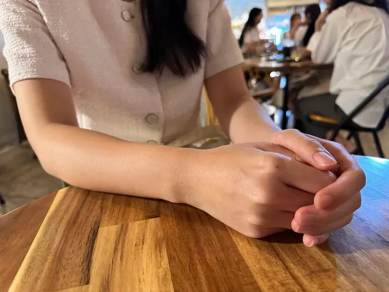 يد تظهران معًا فوق طاولة خشبية، في خلفية غير واضحة لمكان عام، تعبر عن القلق والتوتر الناتج عن تجربة مضايقات رقمية.