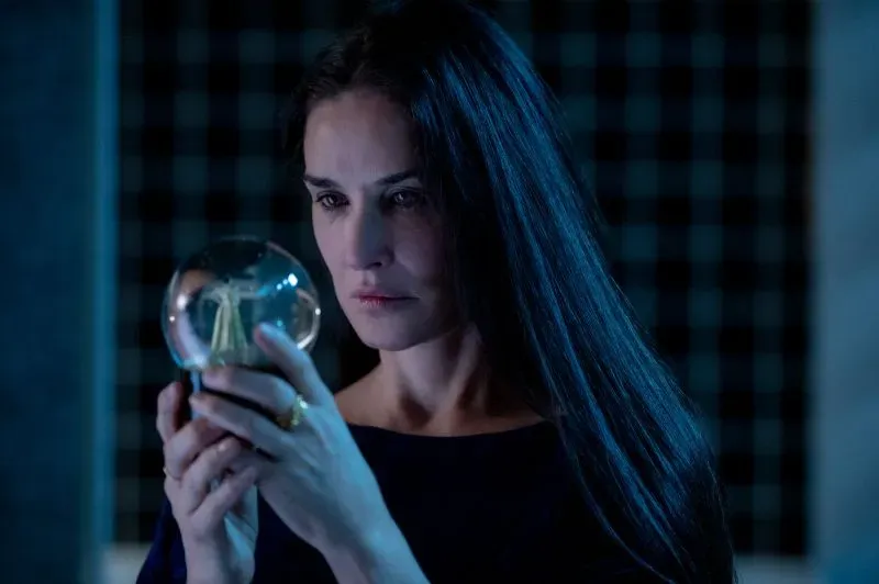ديمي مور تحمل كرة زجاجية في مشهد من فيلم "المادة" (2024)، حيث تستكشف موضوعات كراهية النساء والتمييز على أساس السن.