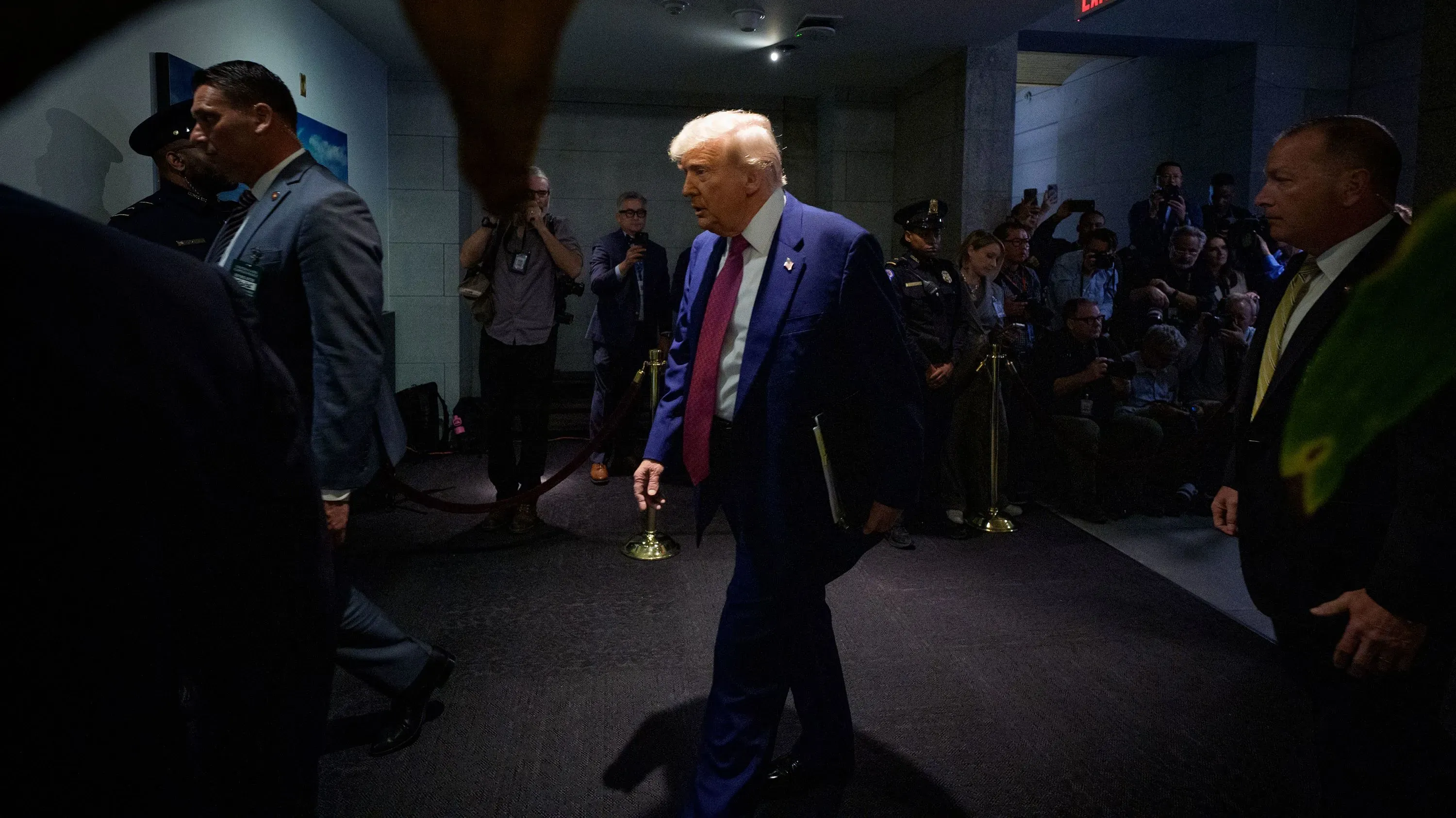 ترامب يسير في ممر مع حراسه، وسط حشد من الصحفيين، بعد حديث عن تخفيضات تمويل مشاريع الفيضانات في الولايات الزرقاء.