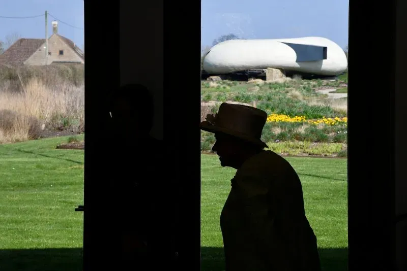 صورة تُظهر silhouette لامرأة ترتدي قبعة، تتجه نحو مدخل جناح معمارية في حدائق كنسينغتون، مع تصميم حديث في الخلفية.