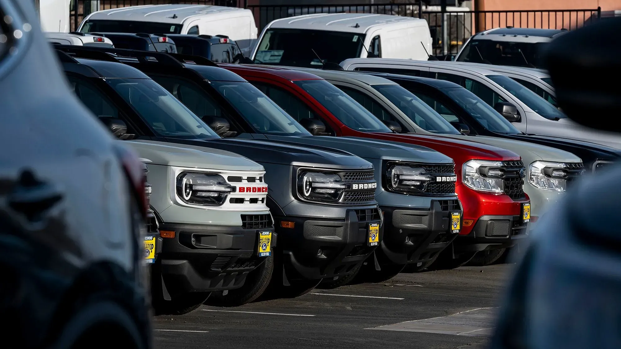 صف من السيارات الجديدة بألوان متنوعة في موقف سيارات، مما يعكس تأثير التعريفات الجمركية على أسعار السيارات وطلب المستهلكين.