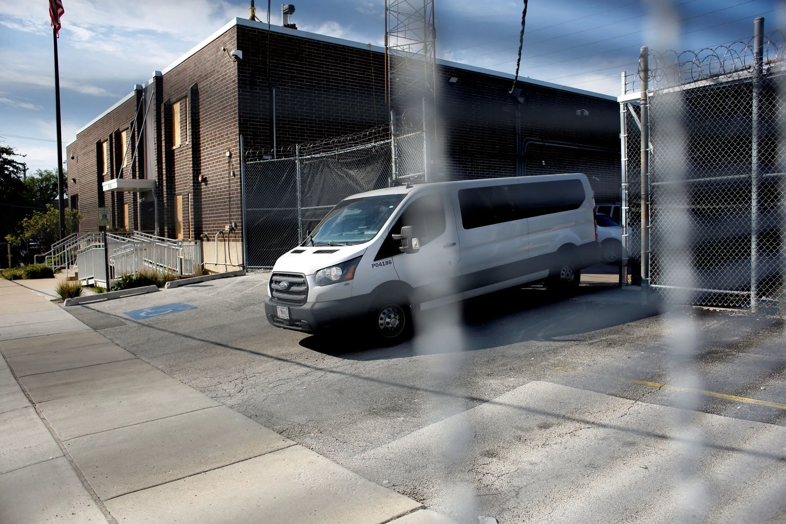 مركبة بيضاء متوقفة أمام مركز احتجاز محاط بأسوار شائكة، تعكس التوترات المتعلقة بالهجرة في الولايات المتحدة.