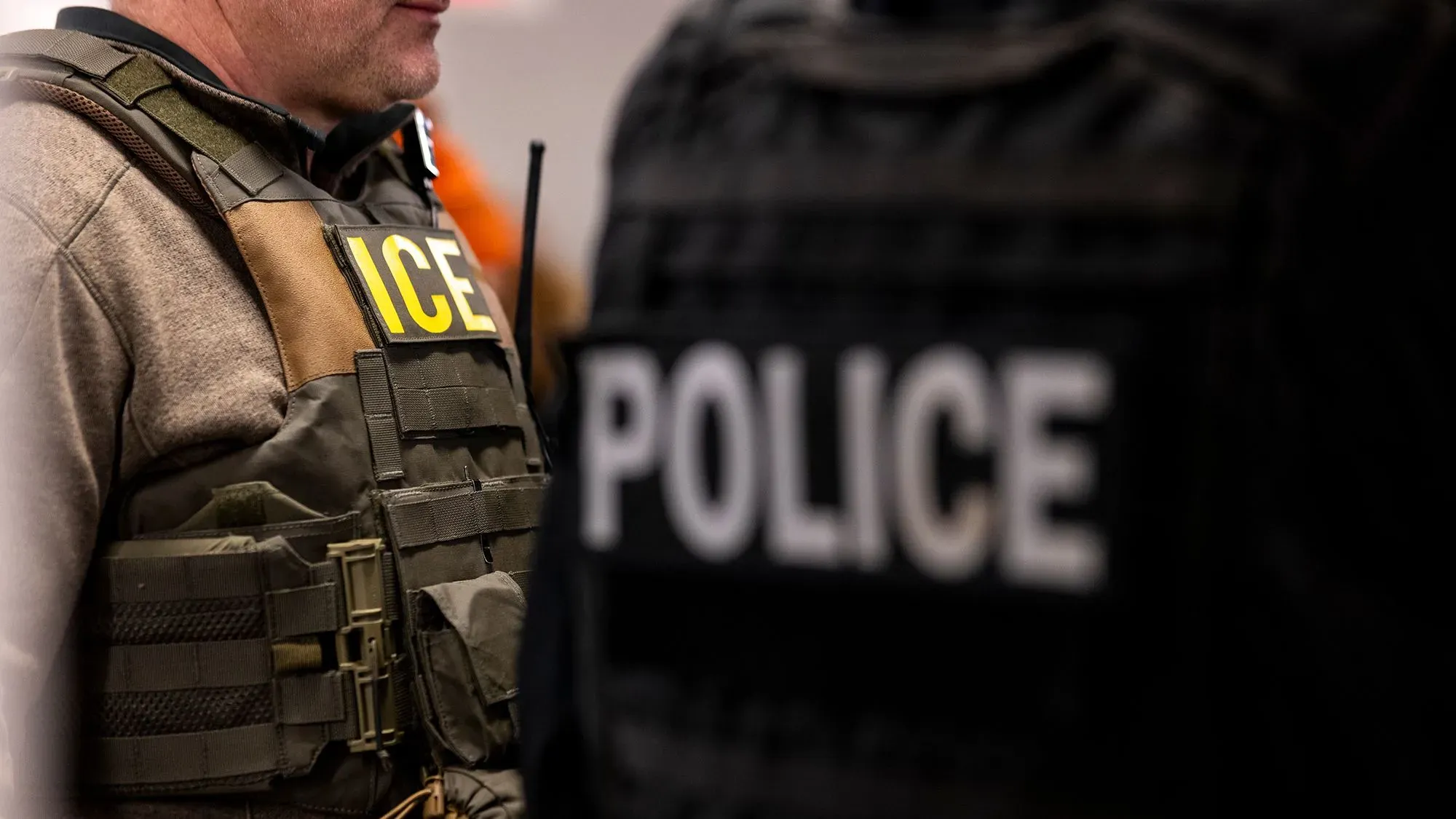 رجال إنفاذ القانون يرتدون سترات تحمل علامات "ICE" و"POLICE"، في سياق مداهمات الهجرة في مواقع العمل.