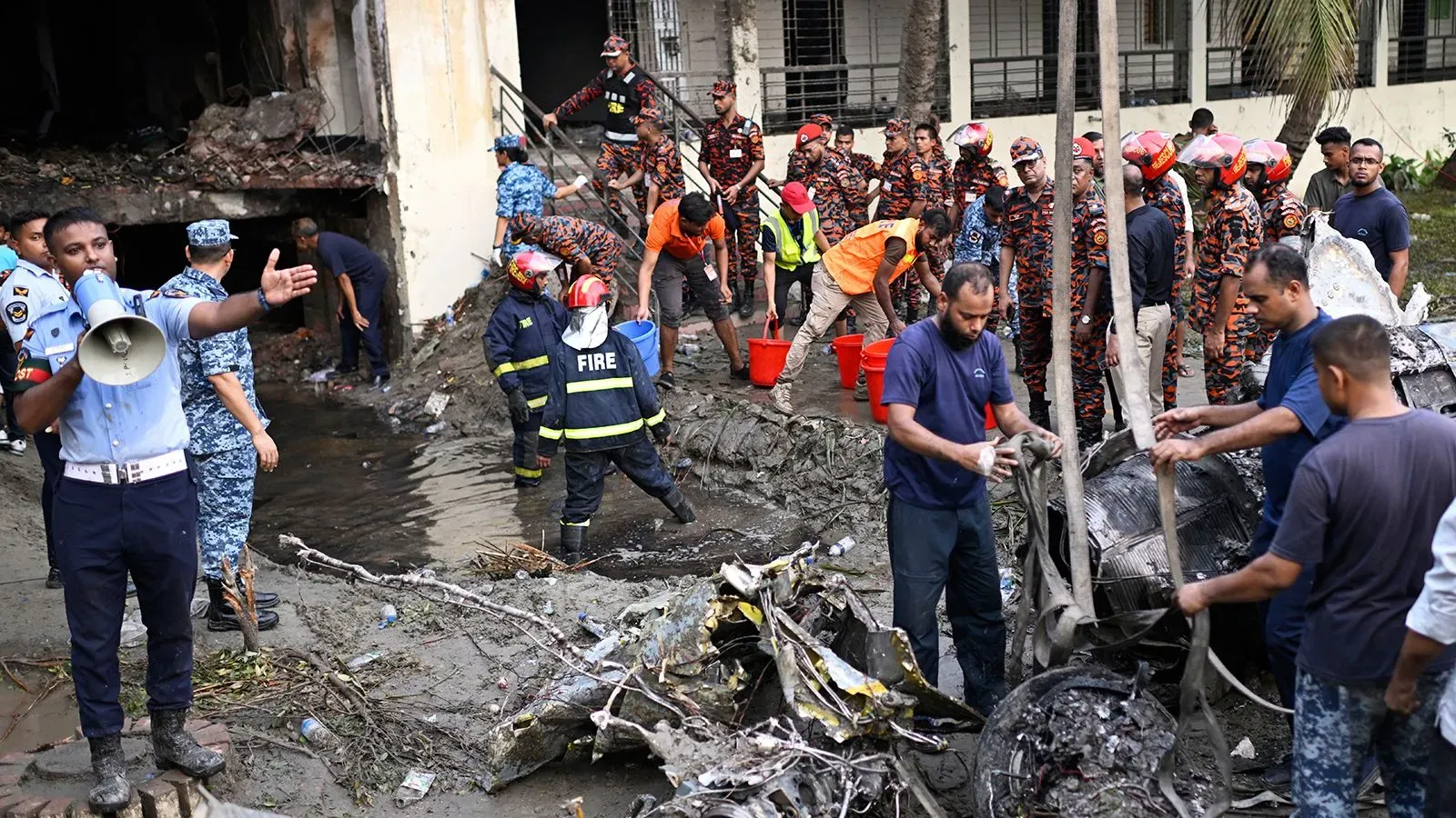 تجمع فرق الطوارئ والشرطة في موقع تحطم الطائرة بالقرب من المدرسة المحترقة في دكا، حيث يعملون على انتشال الحطام.