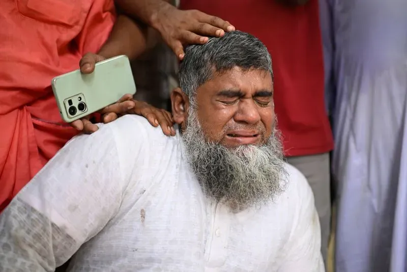 رجل يبكي بحزن شديد بعد حادث تحطم طائرة في دكا، حيث فقد العديد من الأطفال في الحادث، وسط مشاعر الألم والصدمة.