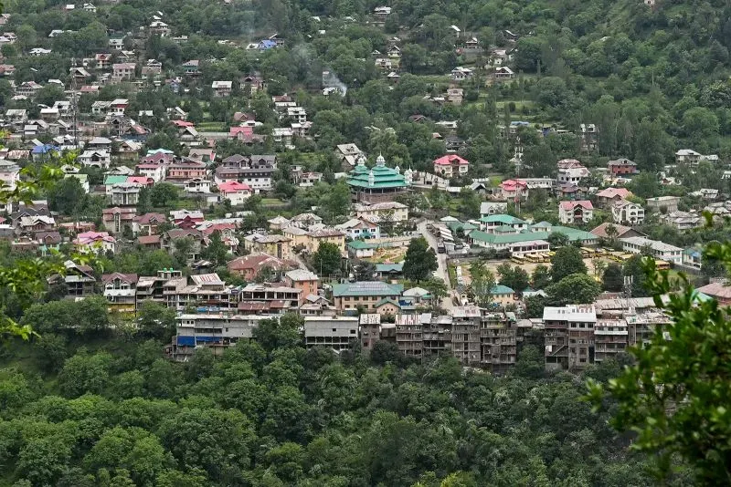 منظر بانورامي لبلدة كشميرية محاطة بالأشجار والمروج، تظهر فيها المباني السكنية المتنوعة، تعكس الأجواء المتوترة في المنطقة.