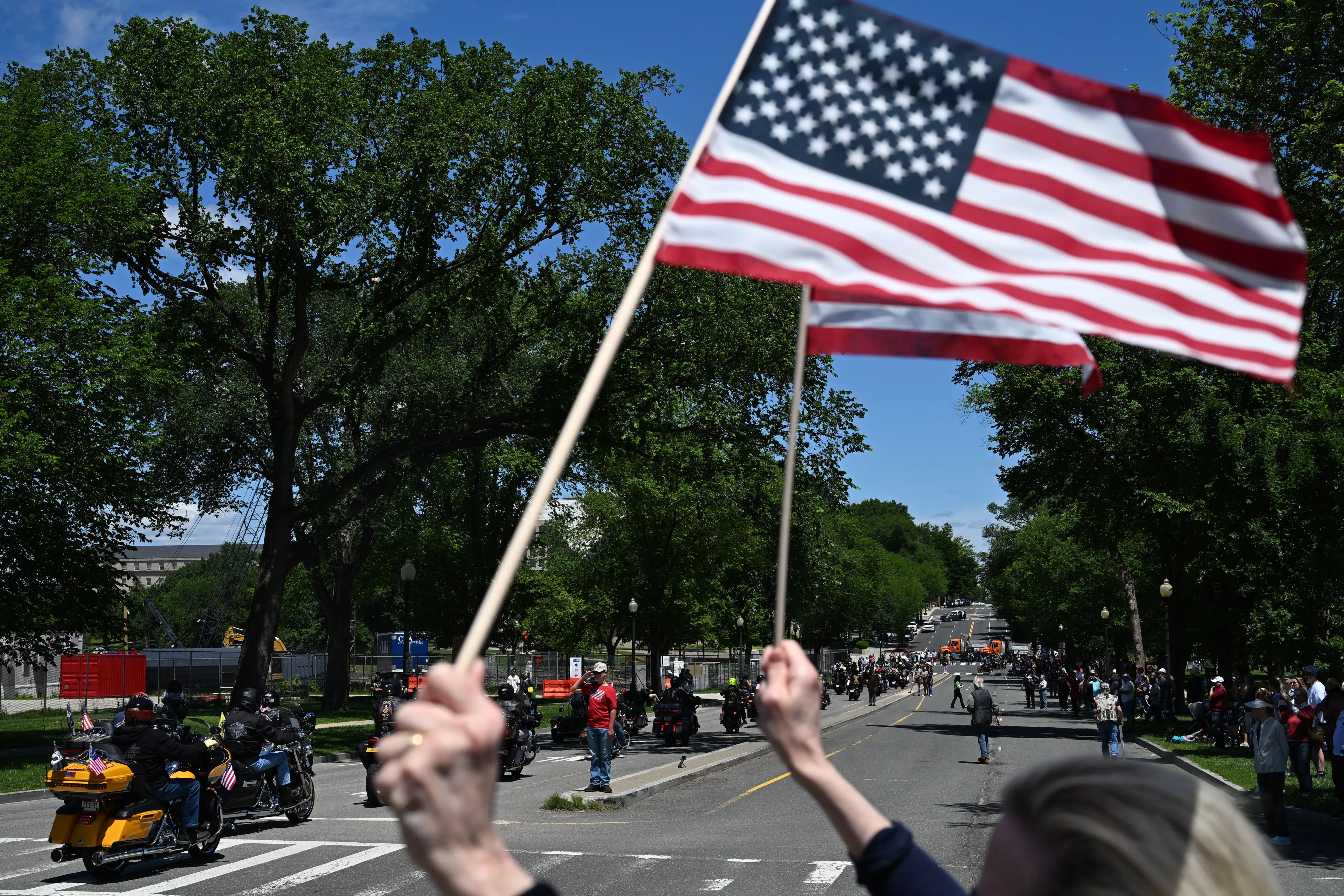 رجل يحمل علم الولايات المتحدة خلال مسيرة لدعم قدامى المحاربين، مع وجود أشخاص ومركبات في الخلفية، تعبيرًا عن التضامن والمساندة.
