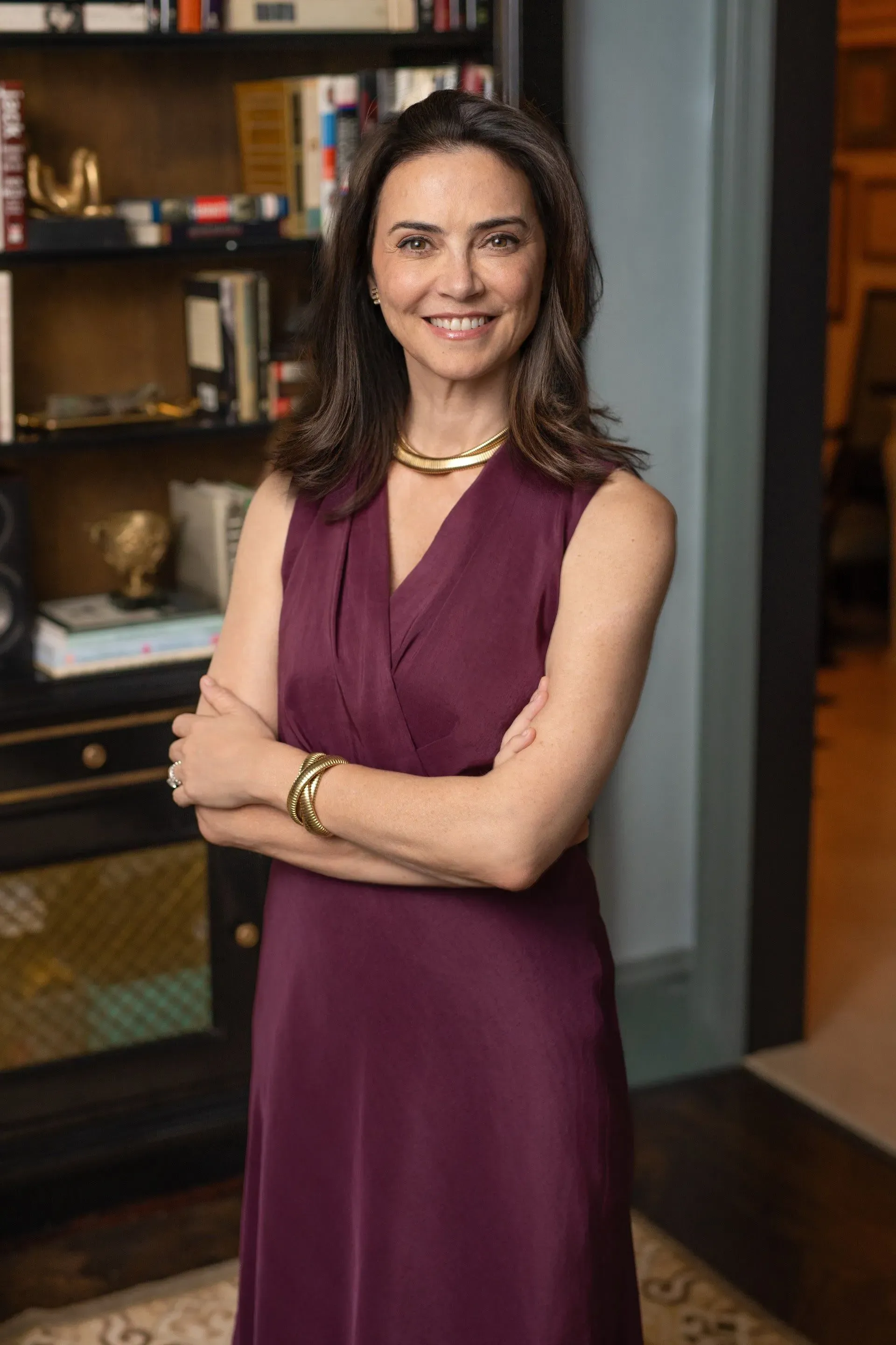 امرأة ترتدي فستانًا بنفسجي وتبتسم، تقف أمام مكتبة مليئة بالكتب، تعكس أهمية التواصل والشعور بالانتماء.