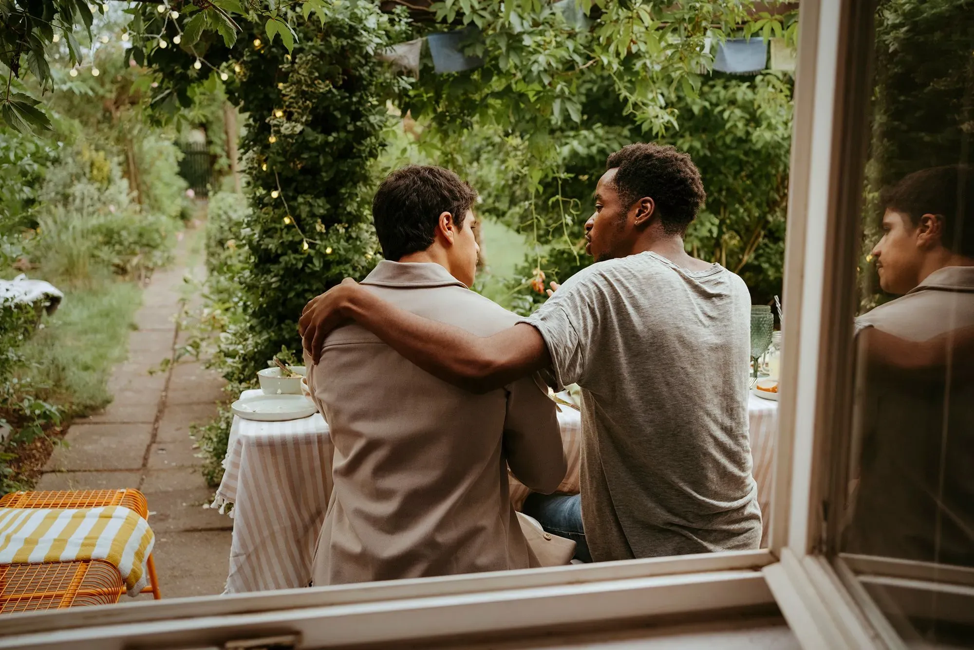 رجلان يجلسان معًا في حديقة، حيث يضع أحدهما يده على كتف الآخر. المشهد يعكس أهمية الروابط الاجتماعية والدعم المتبادل.