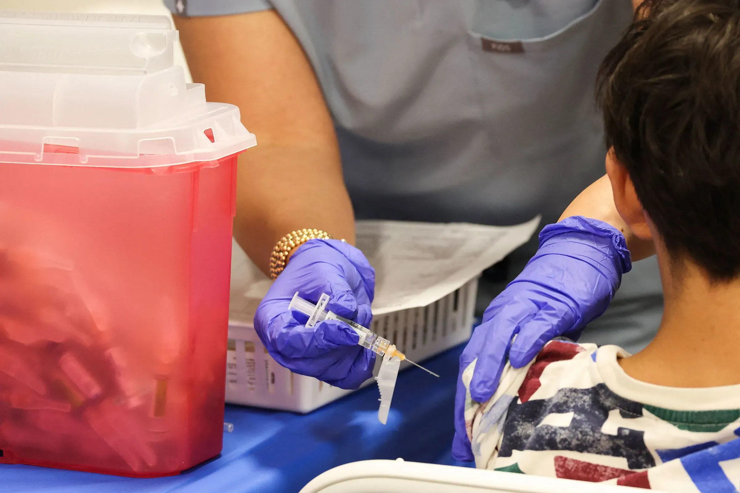 طفل يتلقى لقاحًا في عيادة طبية، حيث تظهر يد ممارس صحي يحمل حقنة، مما يعكس أهمية التطعيمات وفقًا لتوصيات الأكاديمية الأمريكية لطب الأطفال.