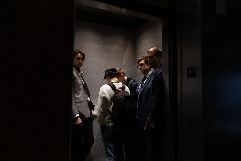 مجموعة من الأشخاص يرتدون ملابس رسمية يقفون في مصعد، مع تعبيرات وجههم الجادة، في سياق أزمة إدارة ترامب لمؤسسة التنمية الأفريقية.