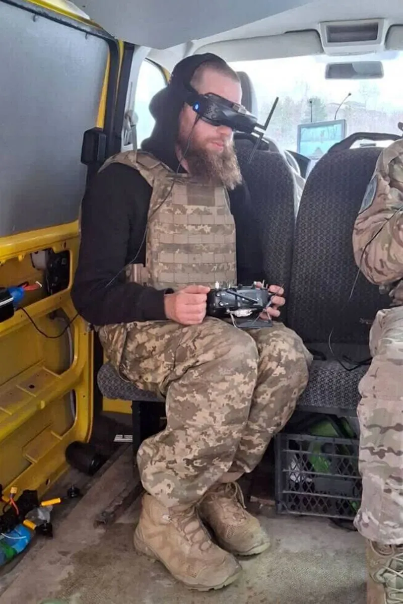 شخص يرتدي سترة عسكرية ويستخدم نظارات تحكم لطائرات مسيرة داخل مركبة، مما يعكس دوره كمشغل طائرات بدون طيار في الجيش الأوكراني.