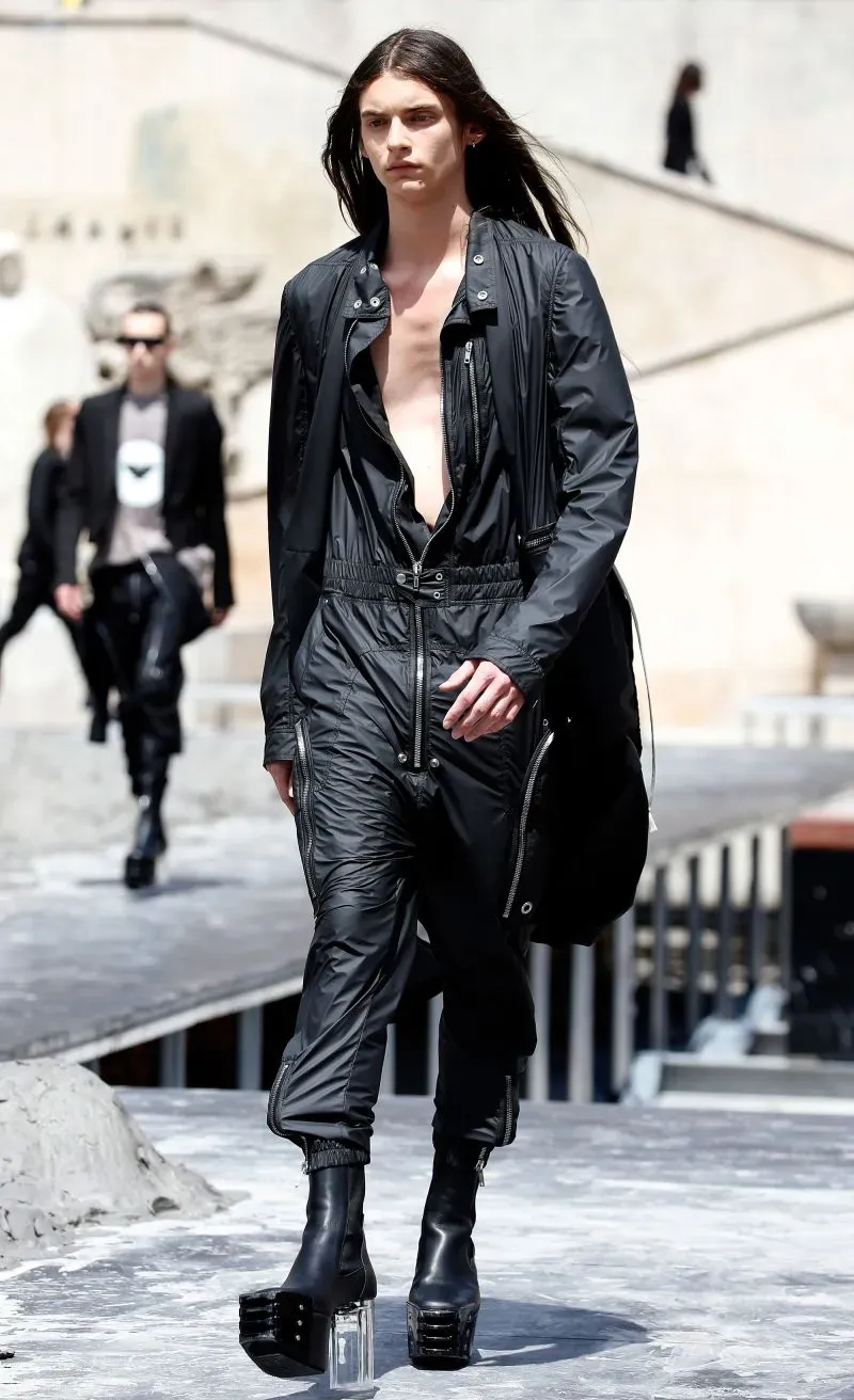 رجل يعرض ملابس عصرية باللون الأسود مع أحذية بكعب عالٍ شفاف، على منصة عرض خلال أسبوع الموضة في باريس.