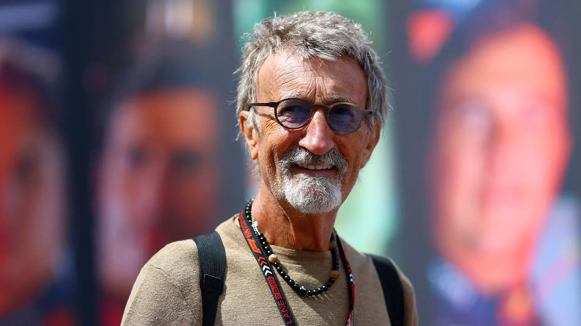 إيدي جوردان، مالك فريق سباق السيارات، مبتسم في حدث رياضي، مع خلفية تضم صورًا لأساطير الفورمولا 1.