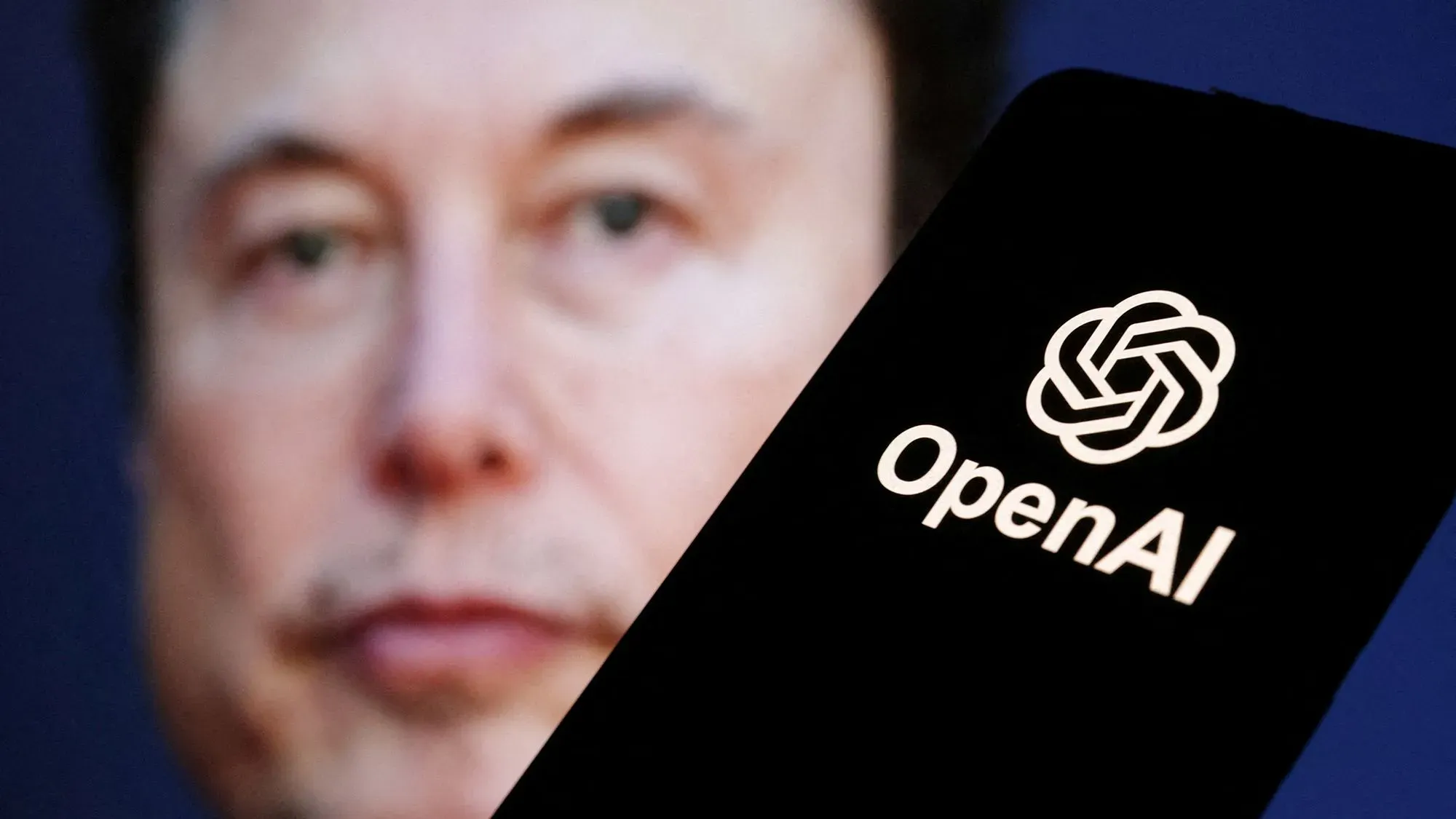 إيلون ماسك يظهر في الصورة مع شعار OpenAI، حيث يتناول مسألة عرض شراء الشركة وسط جدل حول هيكلها غير الربحي.