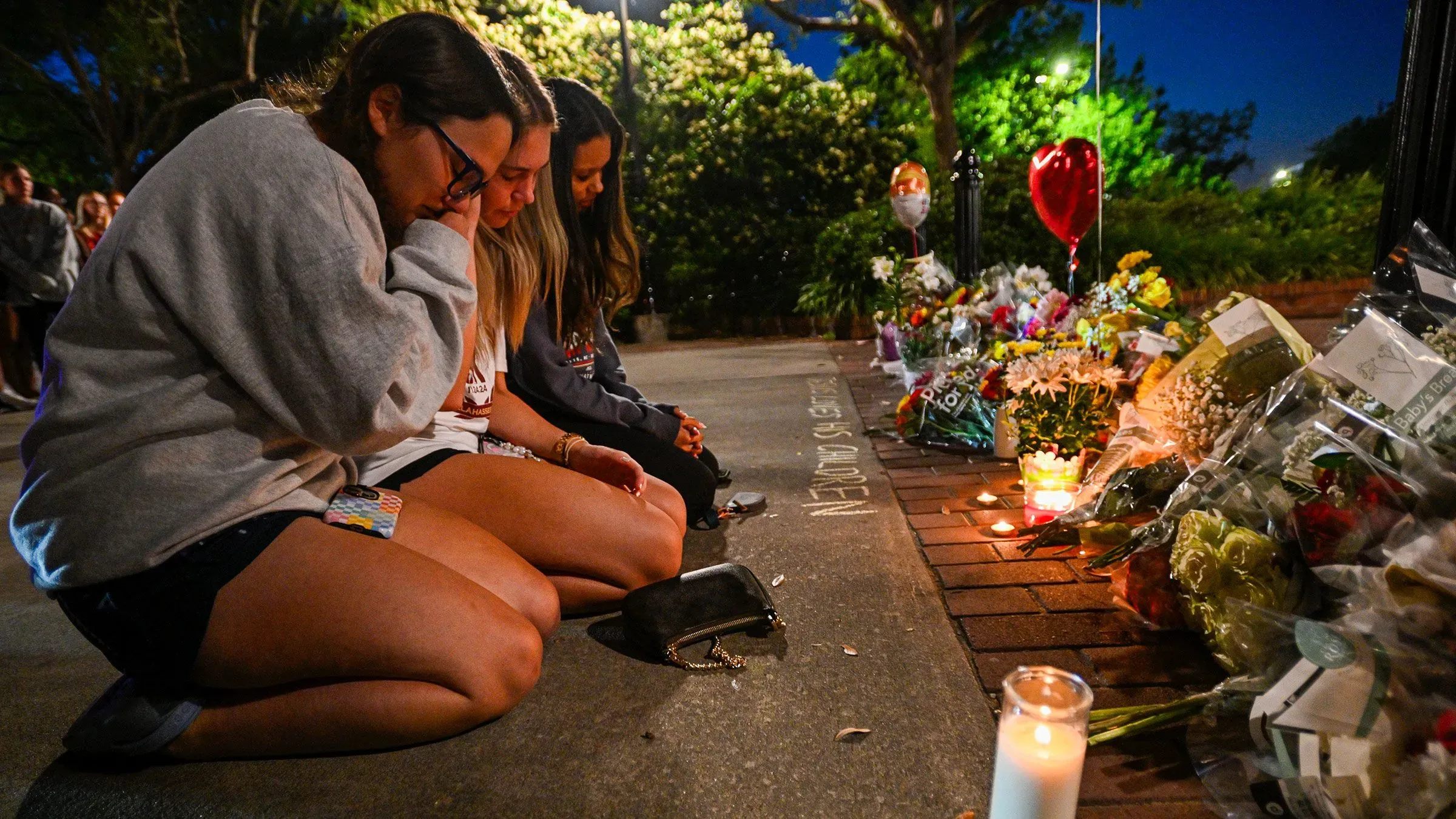 طالبات يجلسن في حزن بجوار أكاليل الزهور والشموع في موقع تذكاري بعد حادث إطلاق نار في جامعة ولاية فلوريدا.