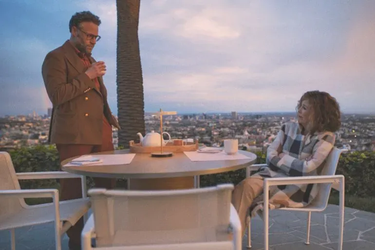 مشهد لممثلين يتحدثان في حوار على طاولة خارجية، مع منظر خلاب لمدينة لوس أنجلوس في الخلفية.