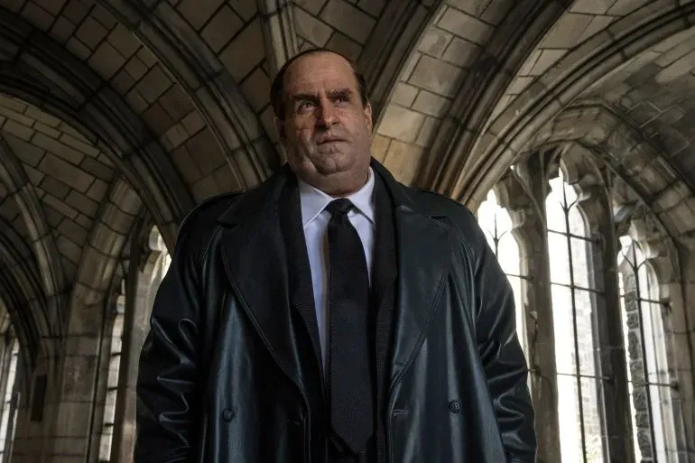 شخصية البطريق، مرتديًا معطفًا أسود، تقف في مكان ذو تصميم معماري مميز، مما يعكس أجواء مسلسل HBO الجديد.