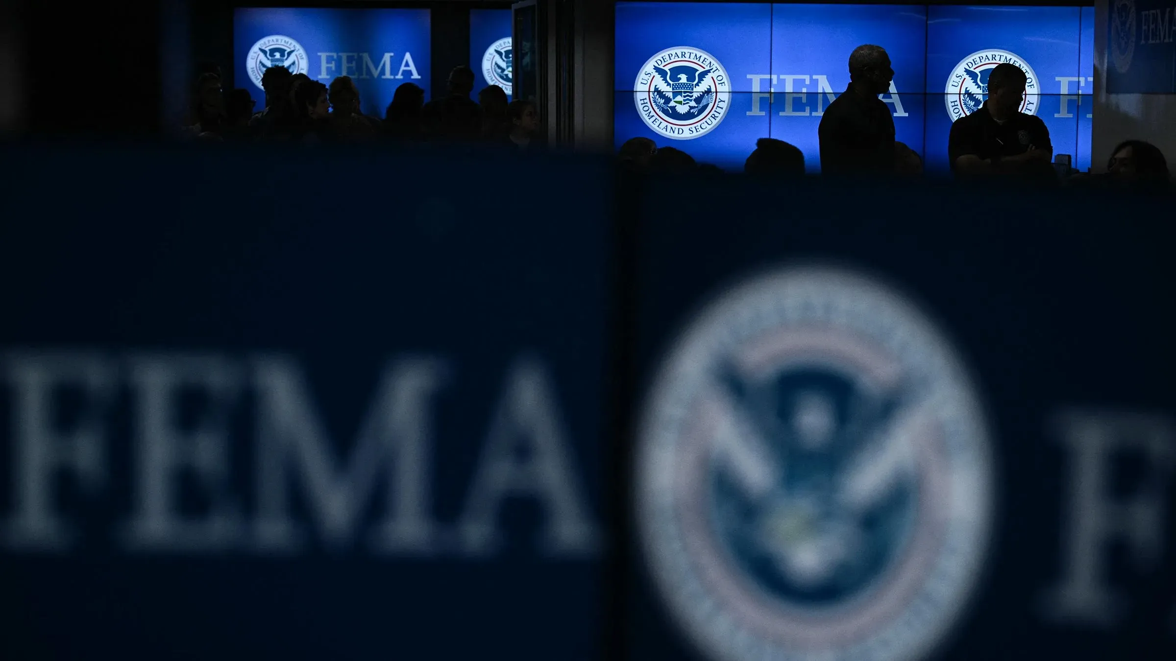 تظهر الصورة موظفين في وكالة إدارة الطوارئ الفيدرالية (FEMA) خلف لافتات تحمل شعار الوكالة، مما يعكس تحديات الاستعداد لموسم الأعاصير.