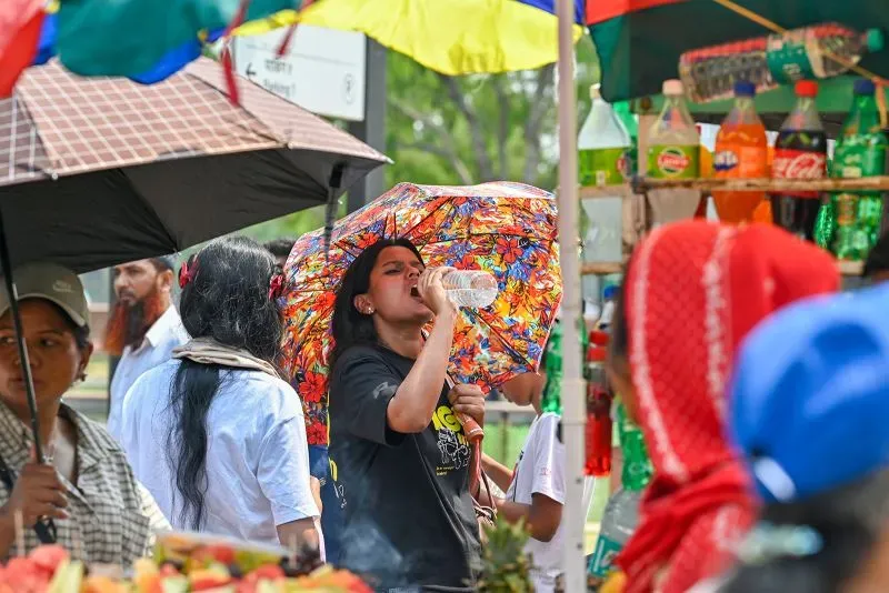 امرأة تشرب الماء تحت مظلة ملونة في سوق مزدحم، تعكس تأثير موجة الحر الشديدة في الهند.