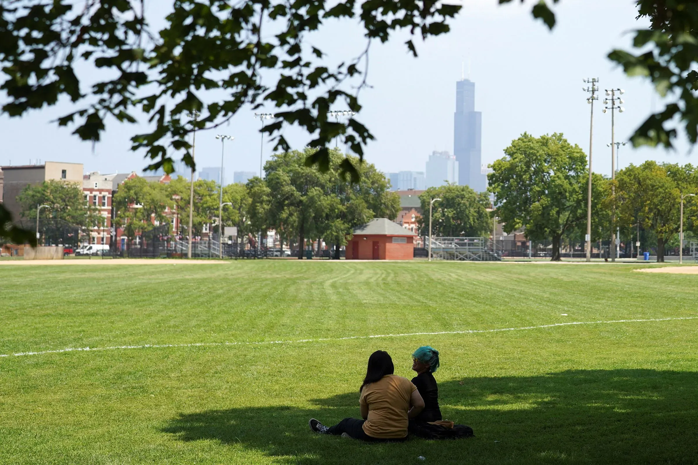 امرأتان تجلسان في حديقة تحت الأشجار، مع منظر لمدينة في الخلفية، تعكس تأثير الحرارة الشديدة على الصحة.