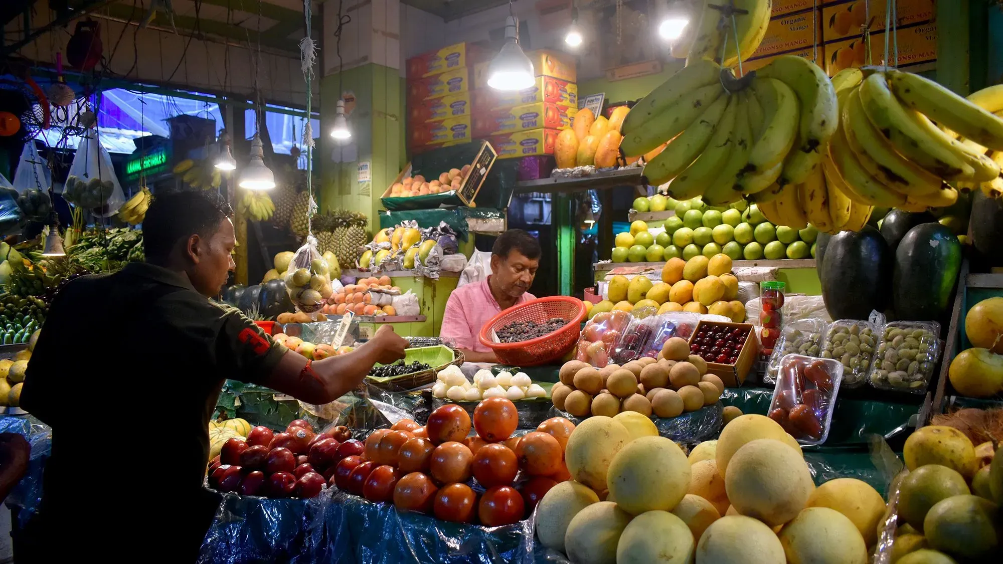 سوق لبيع الفواكه والخضروات مع بائعين يتعاملون مع منتجات متنوعة، مما يعكس تأثير تغير المناخ على أسعار المواد الغذائية.