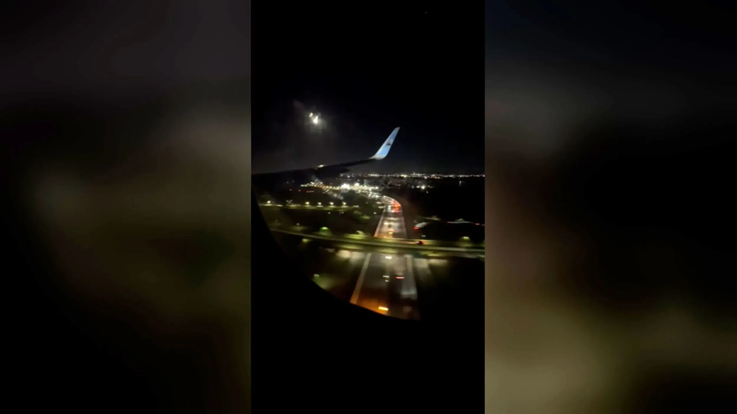 تظهر الصورة منظرًا من داخل طائرة أثناء هبوطها في مطار لويس مارين الدولي، مع أضواء المدينة في الخلفية.