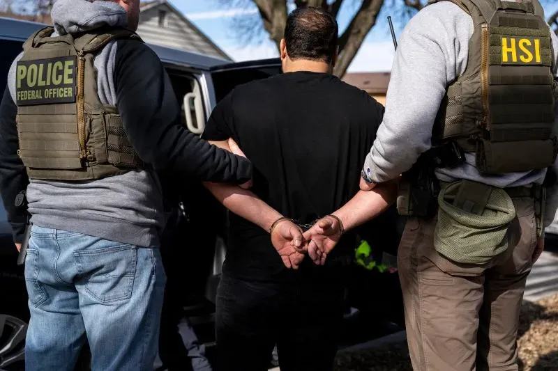 اعتقال شخص من قبل ضباط إنفاذ قوانين الهجرة والجمارك، مع التركيز على إجراءات الترحيل الجماعي في الولايات المتحدة.