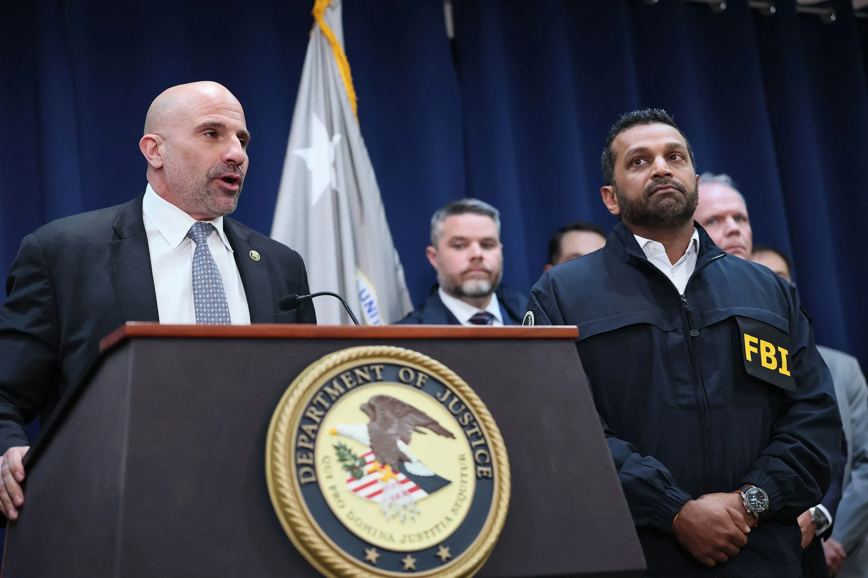 كريستوفر رايا، نائب مدير مكتب التحقيقات الفيدرالي الجديد، يقف بجانب مسؤولين آخرين خلال مؤتمر صحفي، مع شعار المكتب خلفهم.