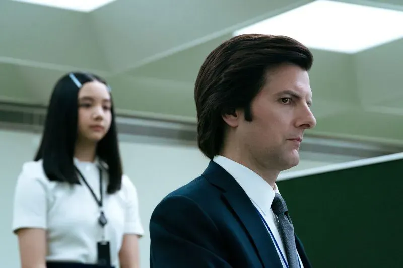 مشهد من مسلسل "Severance" يظهر شخصية مارك س. (آدم سكوت) في وضع جدي، بينما تقف خلفه شخصية أخرى، تعكس التوترات في بيئة العمل.