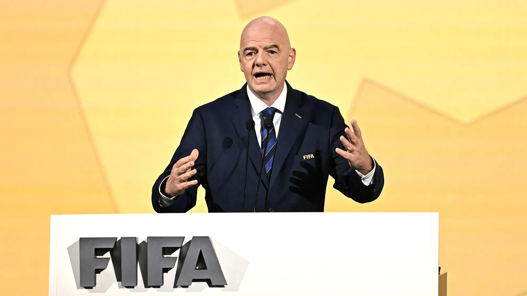 جياني إنفانتينو، رئيس الفيفا، يتحدث في مؤتمر صحفي حول استضافة كأس العالم للسيدات 2023 و2031، مع خلفية صفراء.