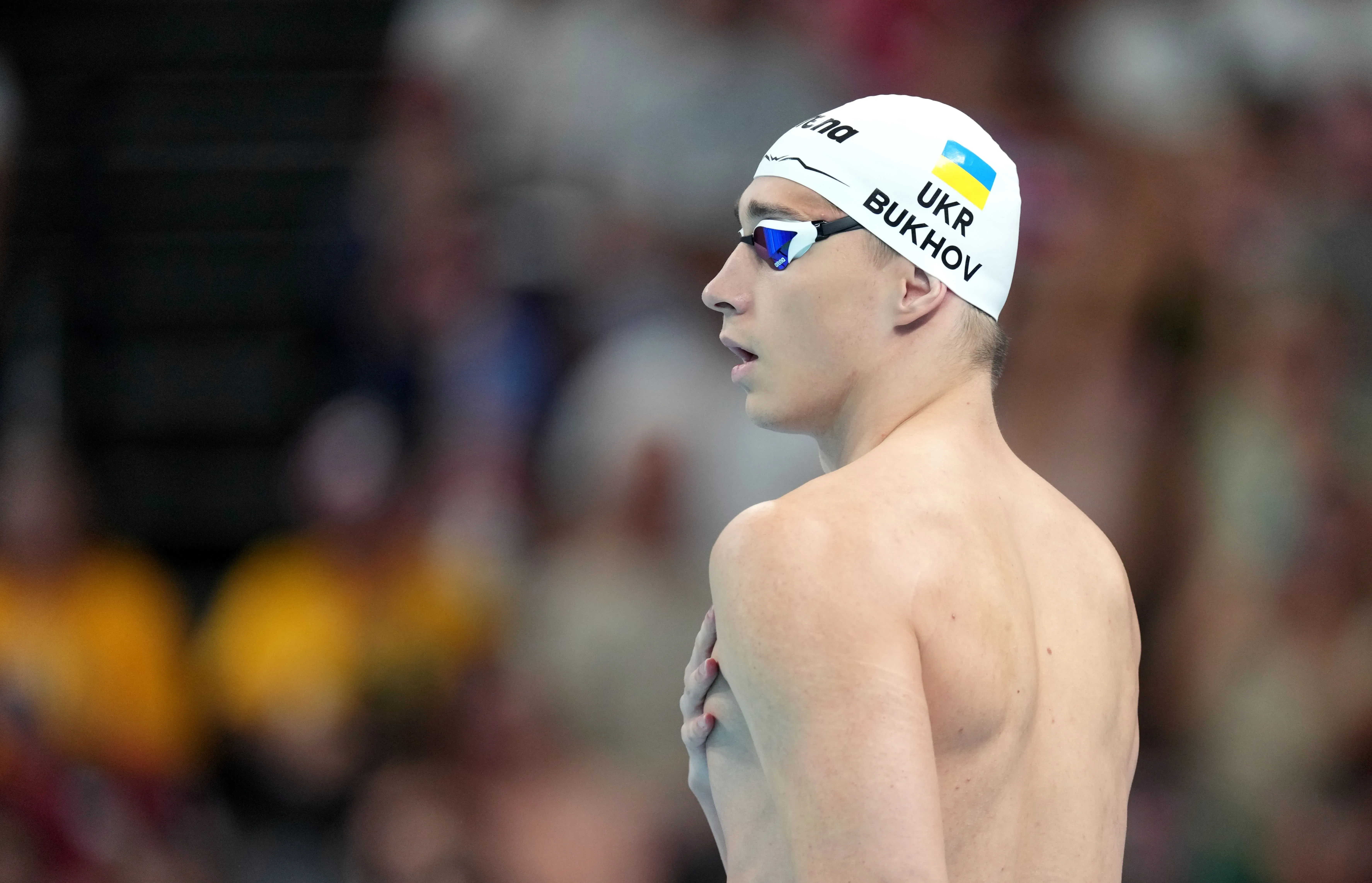 سباح أوكراني يُظهر تركيزه قبل المنافسة، مرتديًا قبعة تحمل علم أوكرانيا، في بطولة العالم للألعاب المائية 2024.