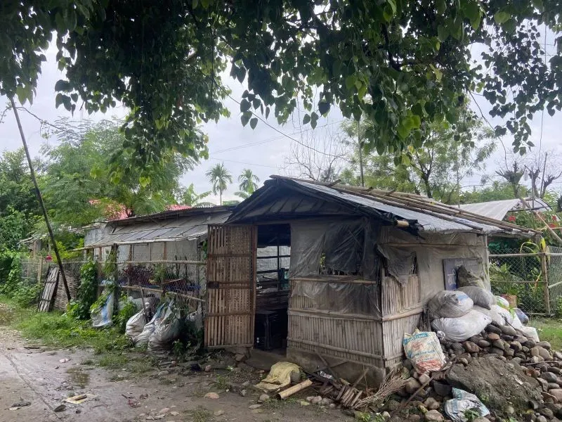 منزل بسيط في منطقة نائية، محاط بالأشجار والنفايات، يعكس الظروف الصعبة التي يعيش فيها اللاجئون العائدون إلى بوتان.