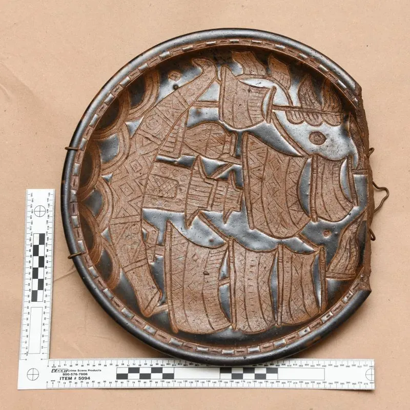 طبق فني مزخرف بتصميم بحري، يظهر تفاصيل دقيقة للسفن، موضوع على خلفية بنية، مع مسطرة توضح الأبعاد.