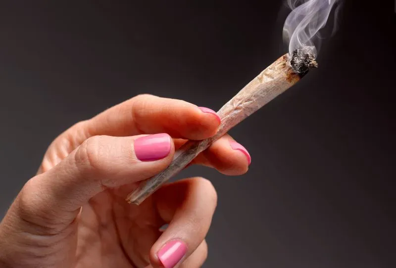 استخدام الماريجوانا أثناء الحمل، مع وجود يد تحمل سيجارة ماريجوانا مشتعلة، يرتبط بزيادة مخاطر الولادة المبكرة وانخفاض وزن المولود.