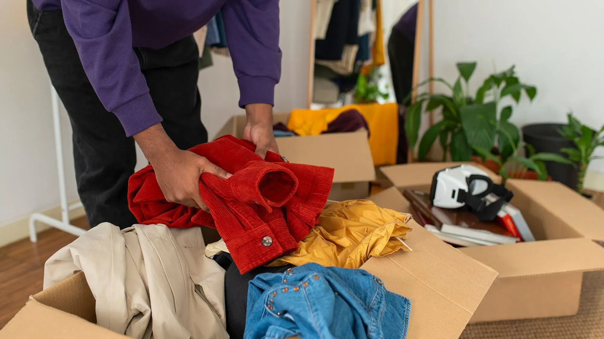 شخص يقوم بفرز الملابس والأغراض في صناديق، يعكس عملية التنظيم والتخلص من الفوضى المنزلية.