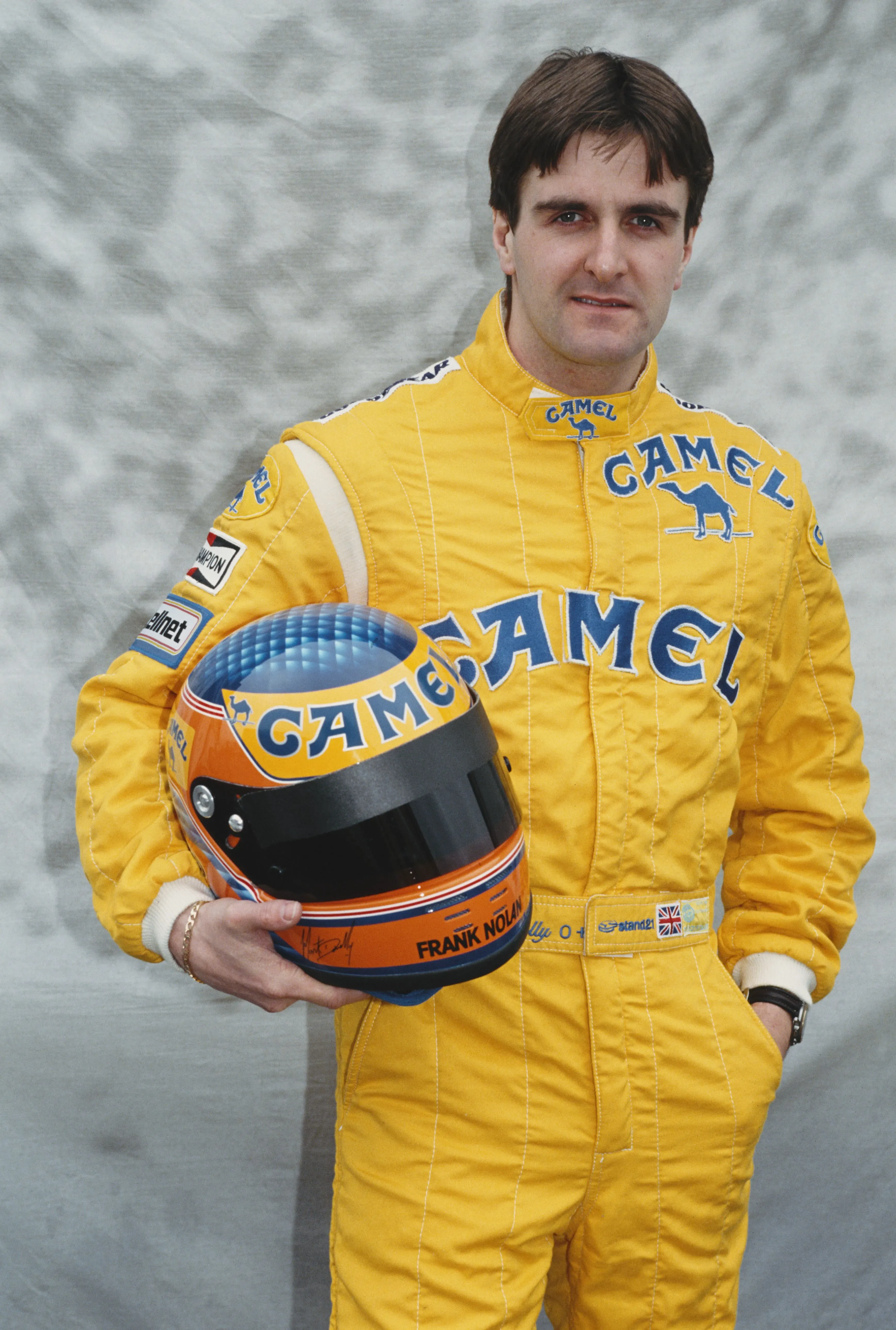 سائق الفورمولا 1 مارتن دونيللي يرتدي بدلة سباق صفراء ويحمل خوذة، مستعرضًا ملامح شجاعة مسيرته بعد حادثه المروع في 1990.